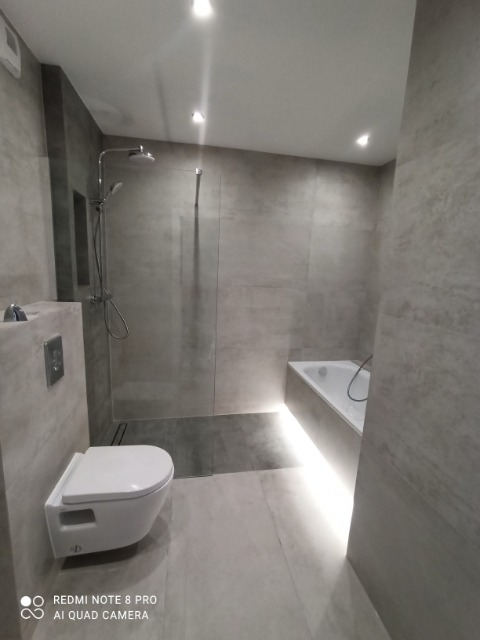 Nowoczesna łazienka w odcieniach szarości z podświetloną wanną i wiszącą toaletą, minimalistyczny design.