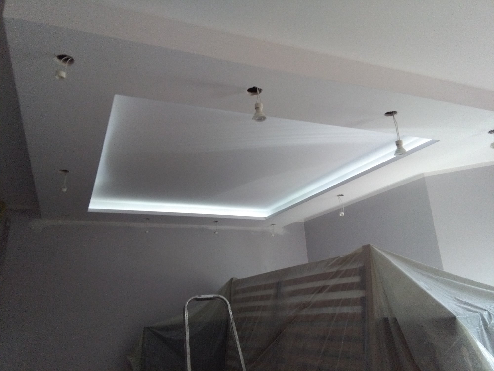 Poddasze po remoncie z podwieszonym sufitem z oświetleniem LED, widoczne niedokończone punkty świetlne i drabina malarska przykryta folią.