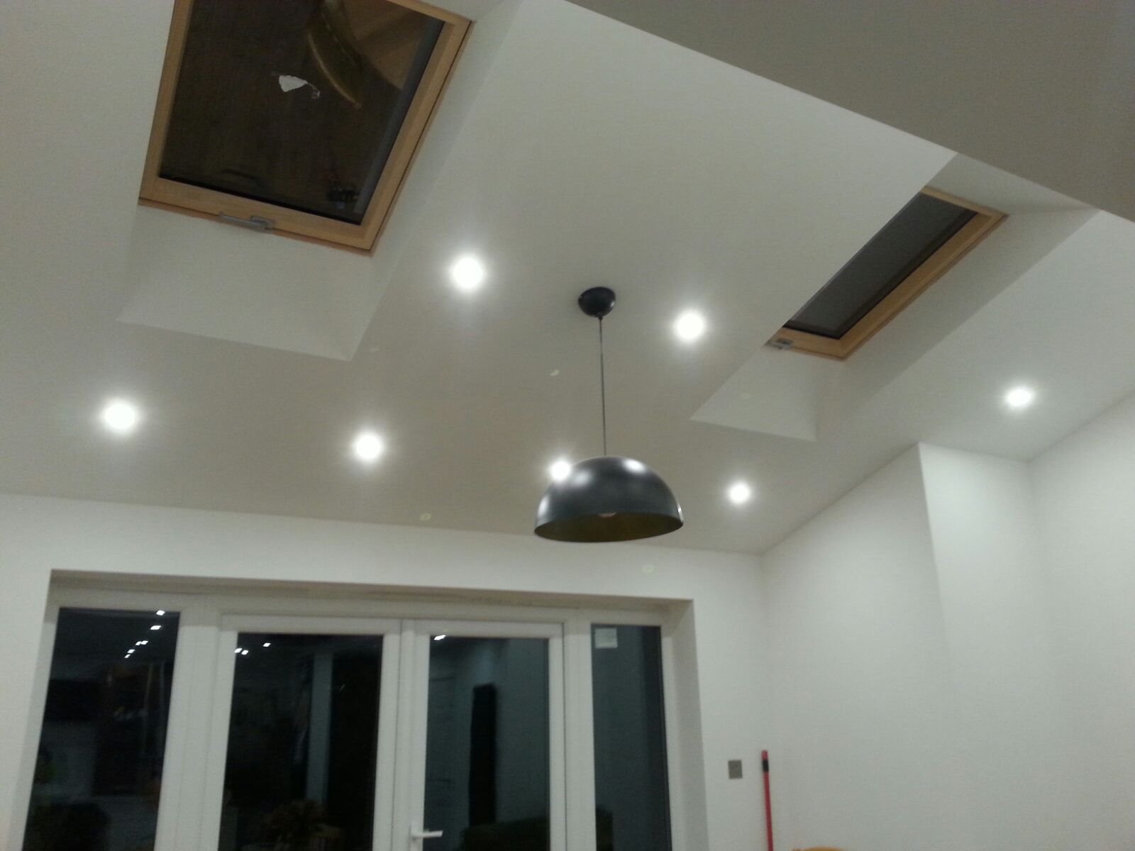 Wykończone wnętrze z dwoma oknami dachowymi w drewnianych ramach, punktowym oświetleniem sufitowym i wiszącą lampą w kształcie kopuły.