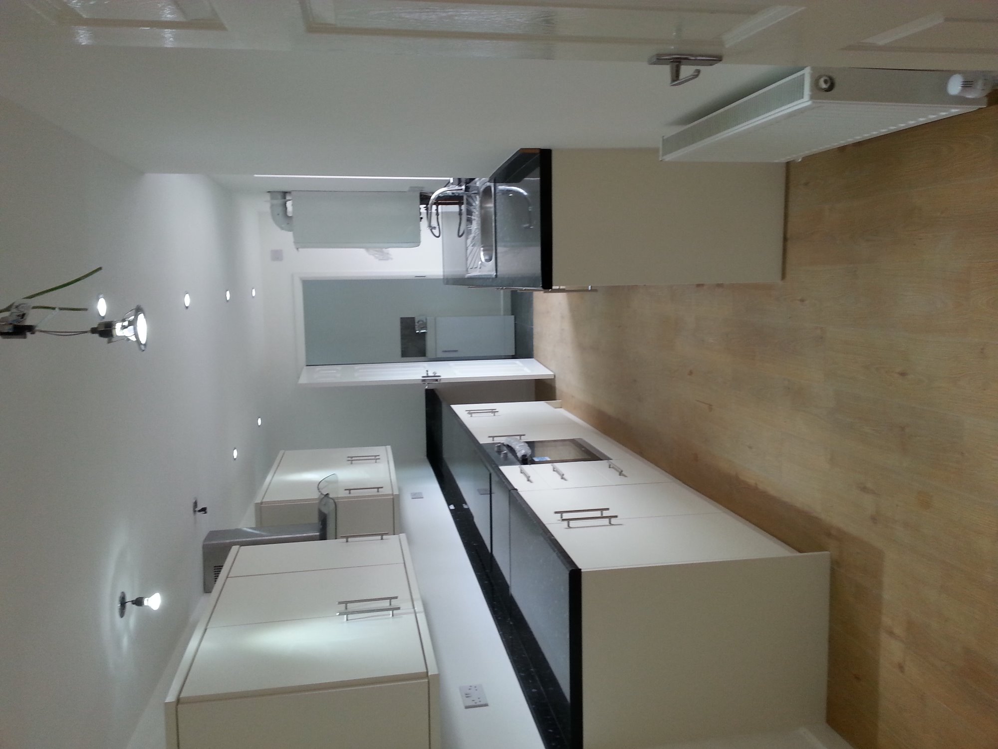 Nowoczesna kuchnia z białymi szafkami i czarnym blatem, widok z perspektywy podłogi, oświetlenie punktowe na suficie, drewniana podłoga.