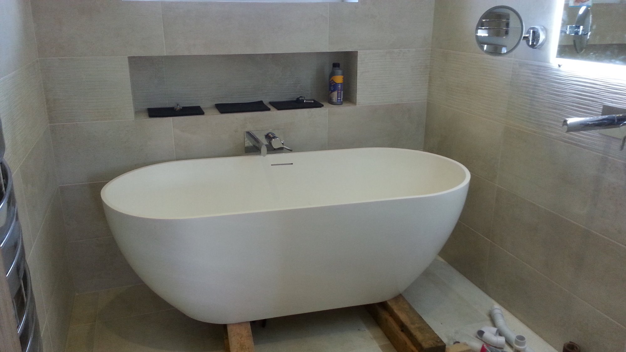 Nowoczesna, wolnostojąca wanna owalna na drewnianych belkach w łazience z beżowymi, poziomymi płytkami i wnęką na akcesoria.