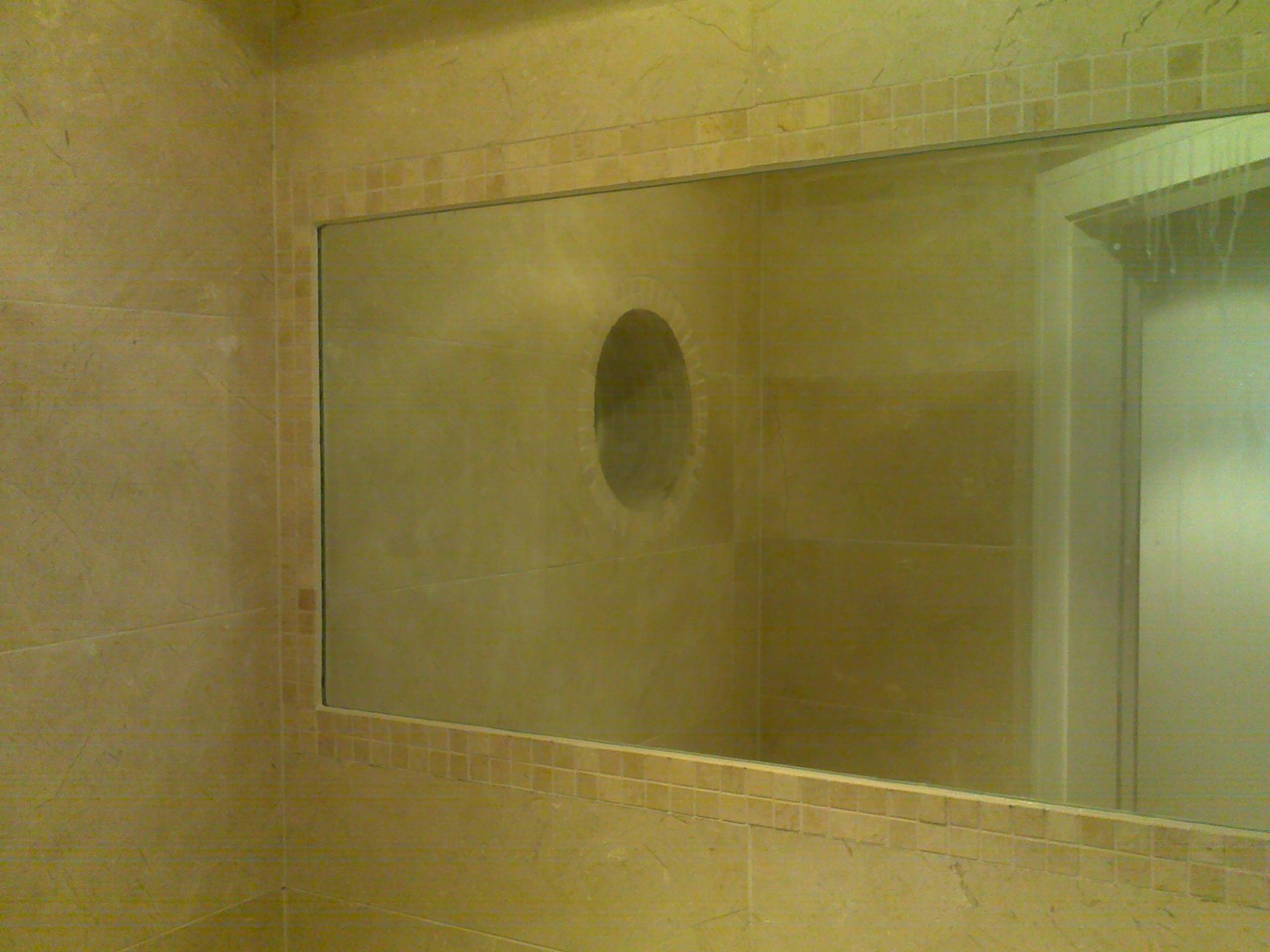Szklana ścianka prysznicowa z owalną wnęką w kremowych płytkach mozaikowych, widok na kabinę prysznicową.