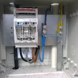 Rozdzielnica elektryczna Apator RBK-00 z zainstalowanymi bezpiecznikami topikowymi, widoczne kable zasilające i uziemiające wewnątrz obudowy.