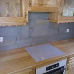 Kuchnia z drewnianymi szafkami, blatem i szarymi płytkami ułożonymi w geometryczny wz&oacute;r, widoczna płyta indukcyjna i piekarnik.