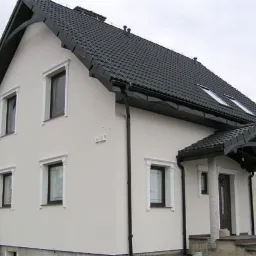 Gotowy dom murowany z białą elewacją, czarnym dachem i ozdobnymi elementami wokół okien.