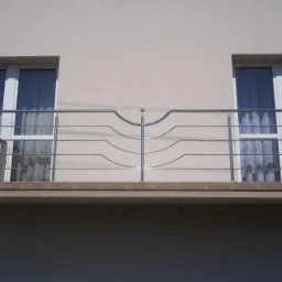 Balkon z nowoczesną, metalową balustradą o falistym wzorze, widok z zewnątrz budynku.