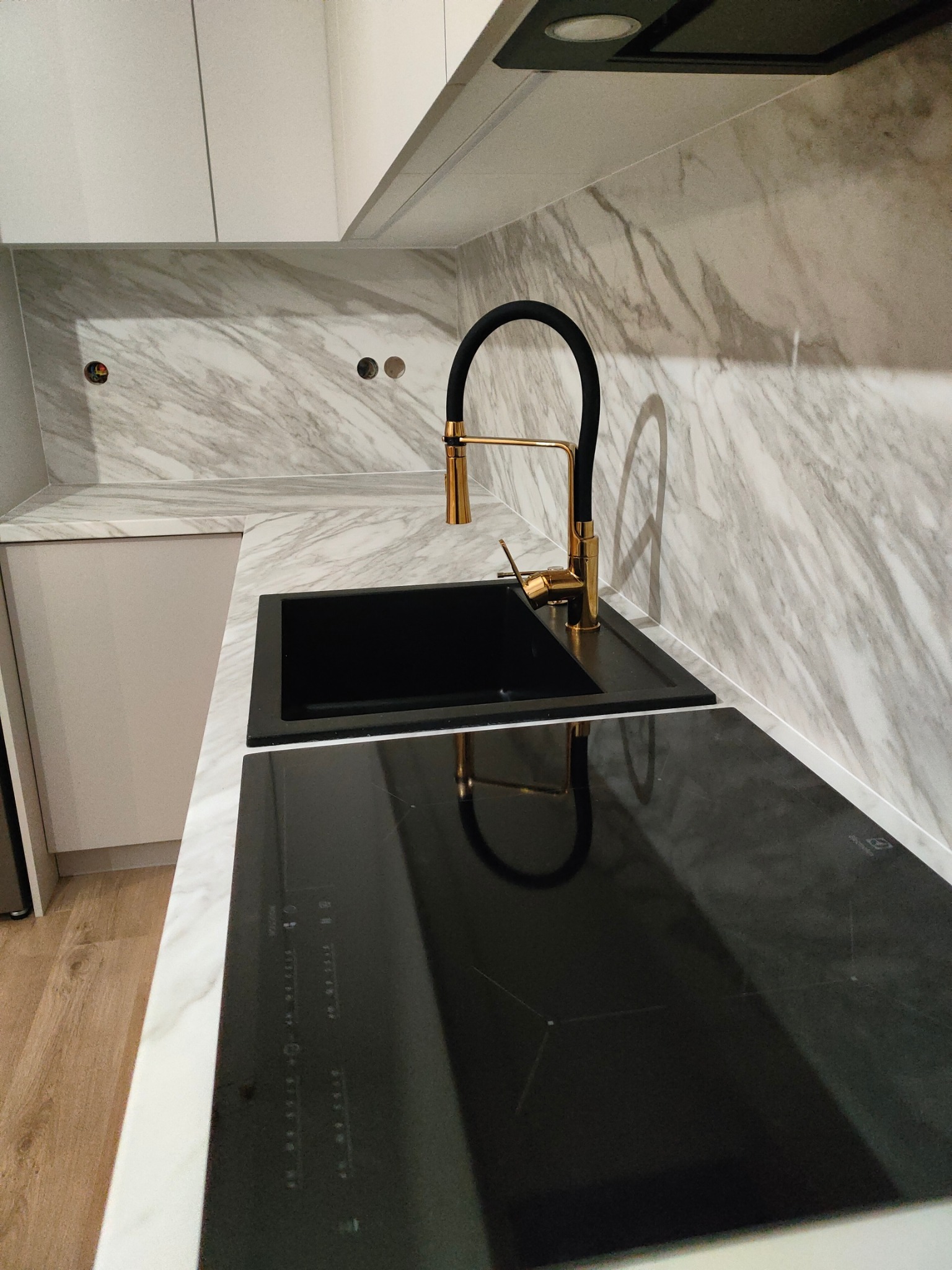 Czarny zlew i złota bateria z czarnym wężem na blacie z imitacją marmuru, obok płyta indukcyjna, widok z góry.