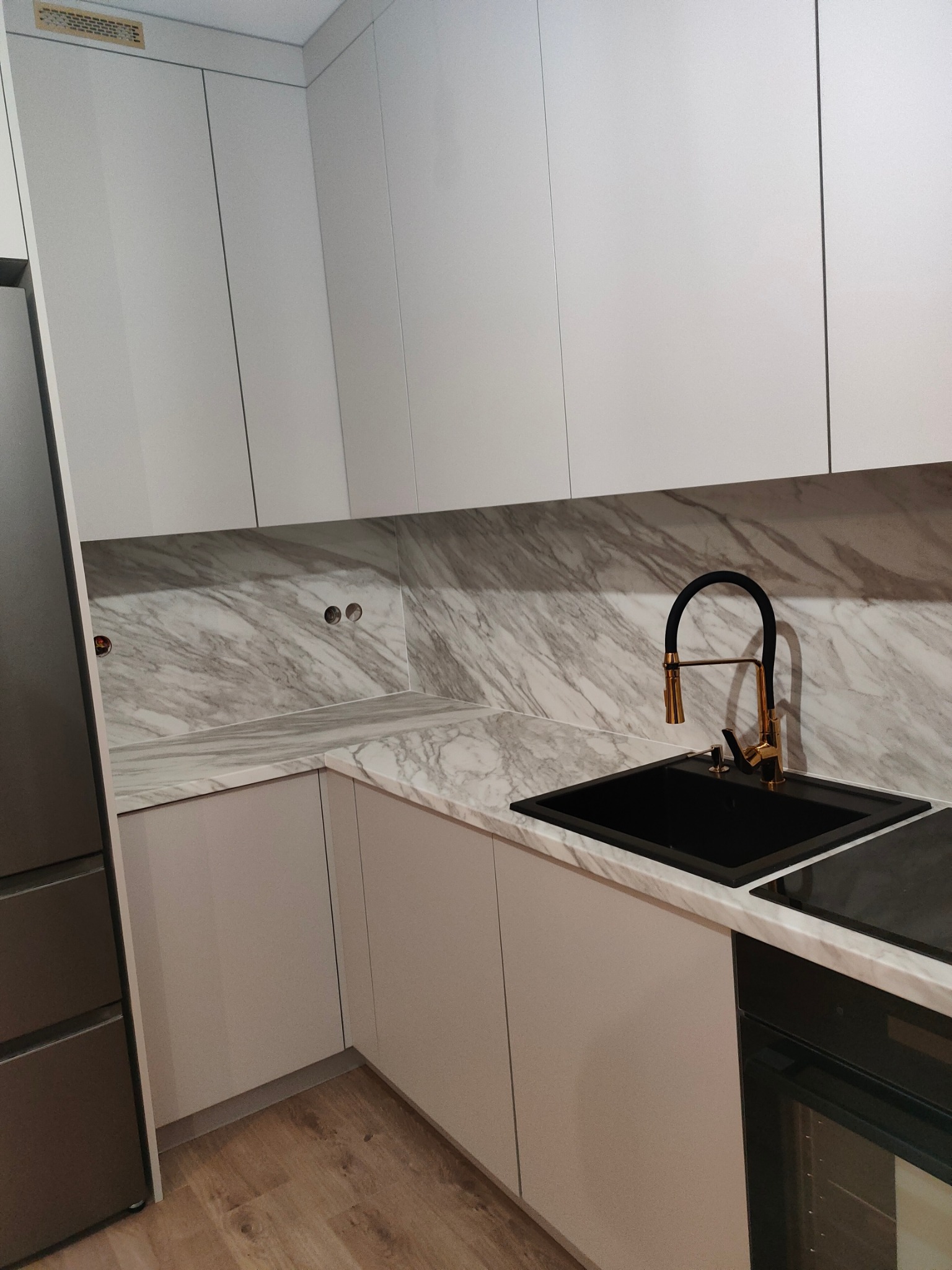 Nowoczesna kuchnia z białymi szafkami, blatem z imitacją marmuru i czarną armaturą z elementami w kolorze złota. Widoczny czarny zlew i płyta indukcyjna.