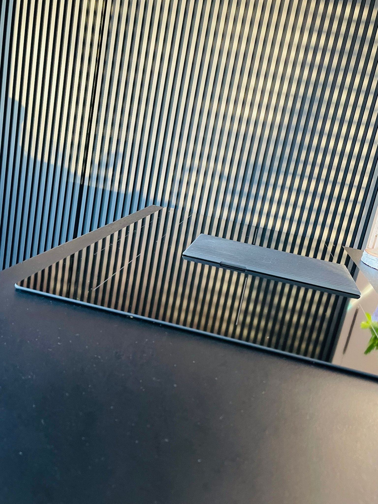 Czarny, błyszczący blat kuchenny z indukcyjną płytą, odbijający pionowe lamele na ścianie. Minimalistyczny design, nowoczesne wykończenie.