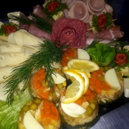 AgawaHouse - Dekoracyjna taca z galaretkami z warzywami, wędlinami ułożonymi w rozety i plastrami sera, całość udekorowana zieleniną.