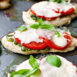 AgawaHouse - Apetyczne filety z kurczaka z pesto, pomidorami i mozzarellą, udekorowane świeżą bazylią, ułożone na ciemnej blasze do pieczenia. Gotowe danie.