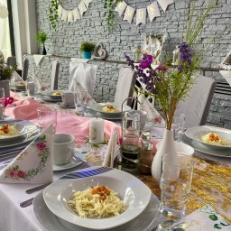 AgawaHouse - Elegancko nakryty stół w Świętochłowicach na komunię: biały obrus, kwiaty, dekoracje, talerze z daniami. Stonowana kolorystyka i dbałość o detale.