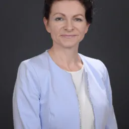 Portret kobiety w jasnoniebieskiej marynarce z ozdobnym zamkiem błyskawicznym na tle szarego studia.