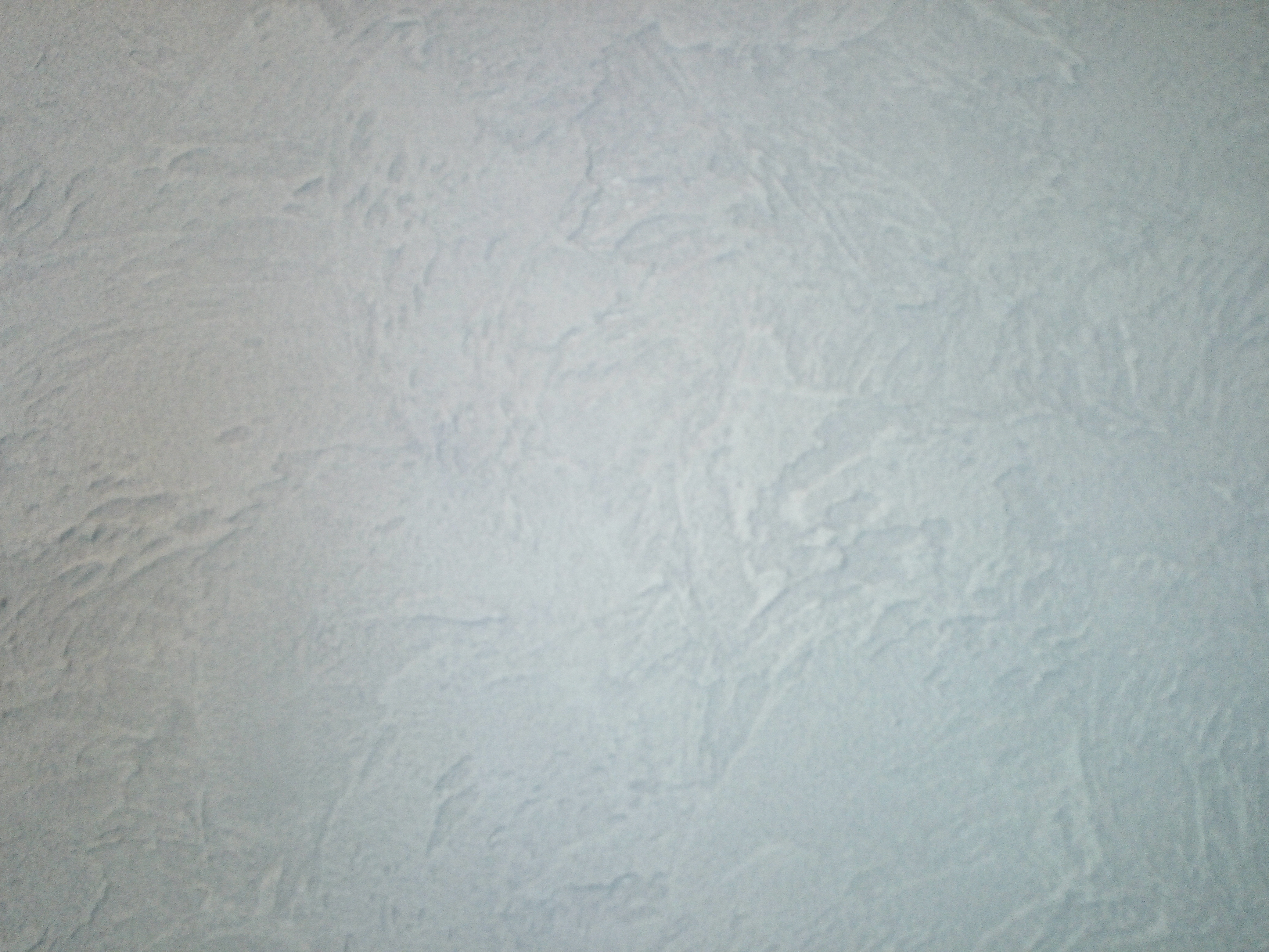 Jasnoszara ściana pokryta dekoracyjną strukturą z efektem delikatnych, nieregularnych wzorów i subtelnych cieni.