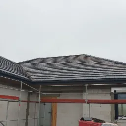 Nowy dach z ciemnej dachówki ceramicznej na budynku w trakcie budowy, widoczne rusztowania i niezakończone prace elewacyjne.