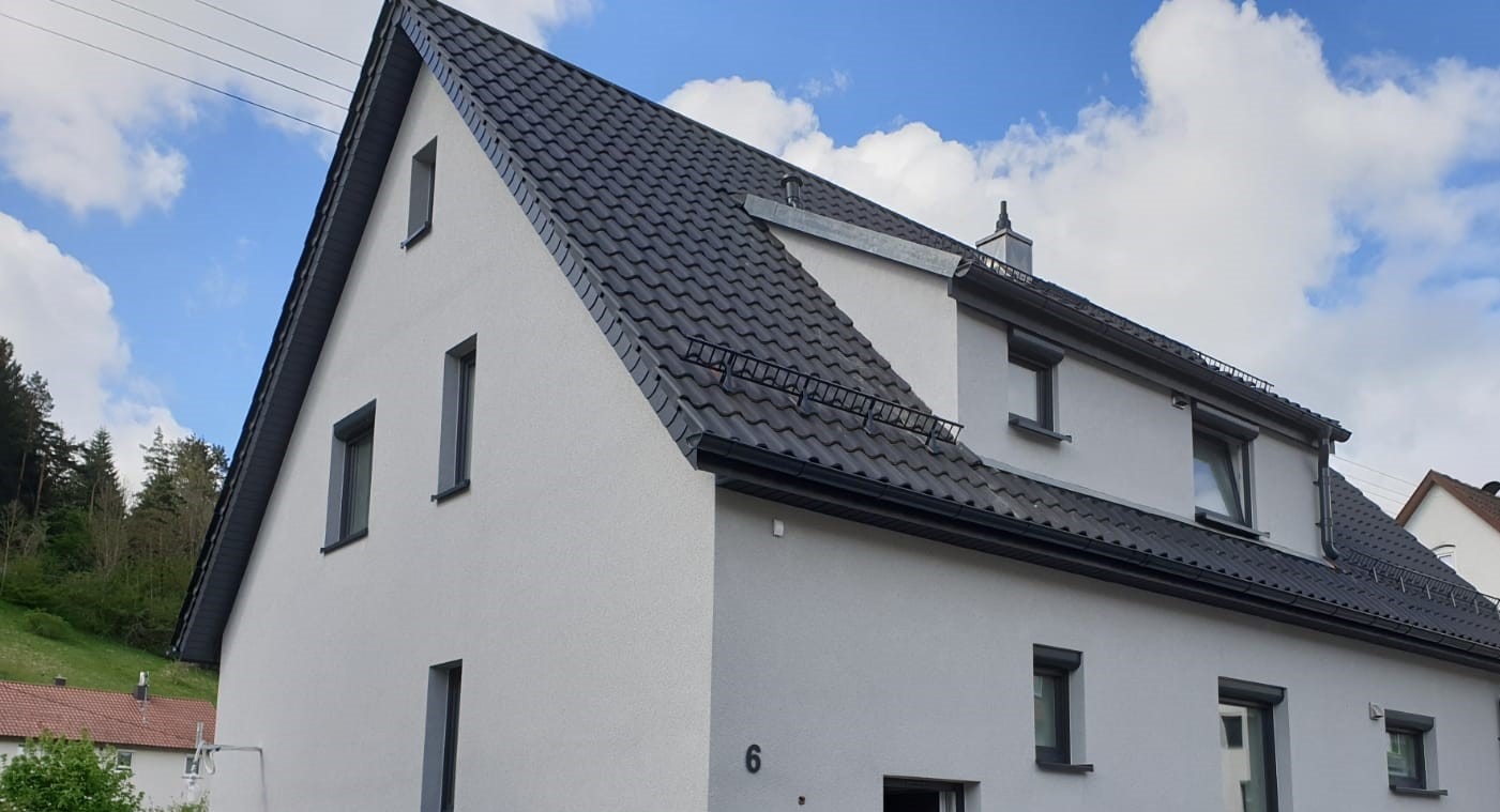 Nowoczesny dom jednorodzinny w Bąkowie z ciemnoszarą dachówką, widoczne obróbki blacharskie i zabezpieczenia przeciwśniegowe na dachu.