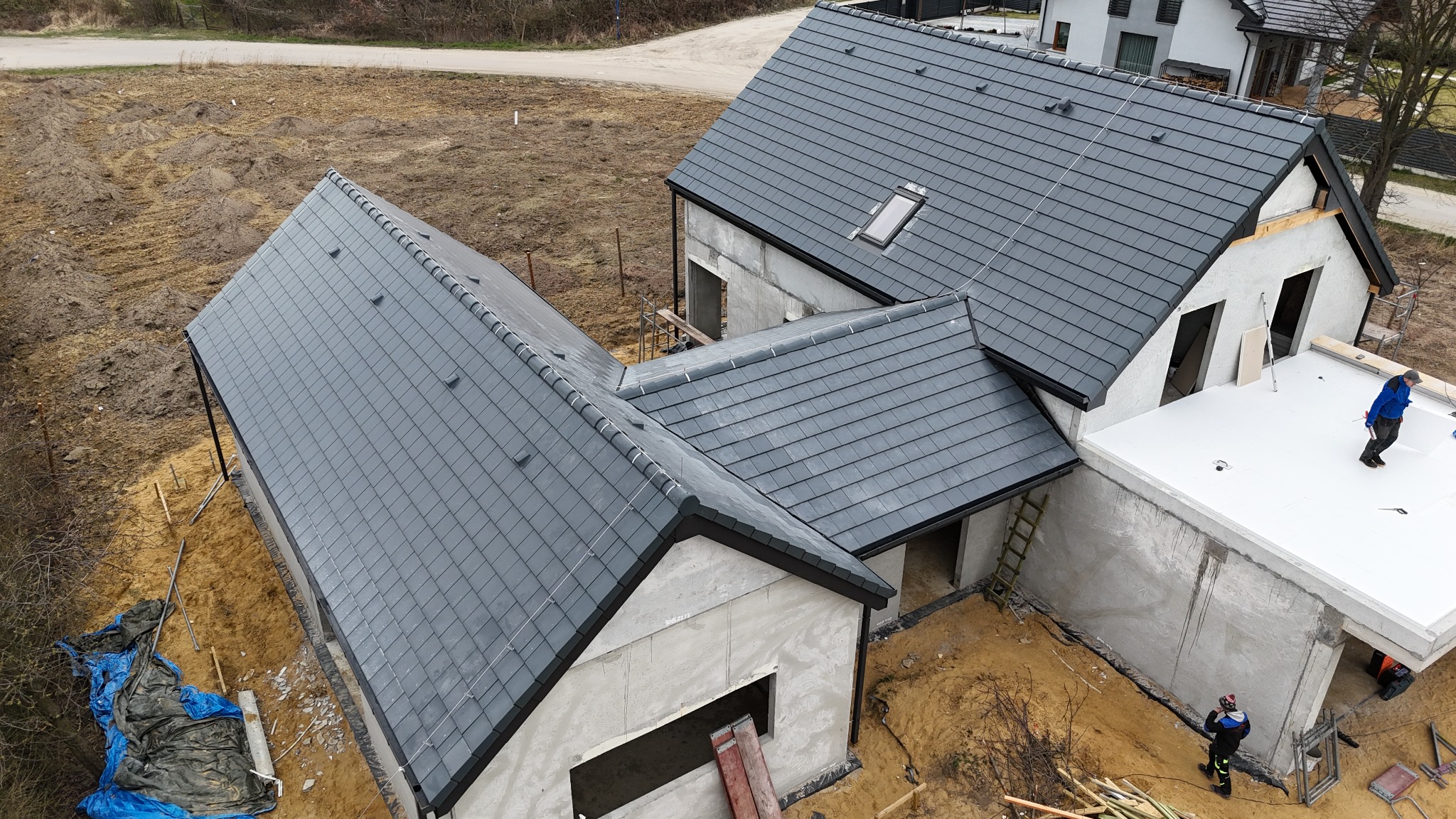 Nowoczesny dom w trakcie budowy z grafitowym dachem z dachówki ceramicznej. Widok z góry ukazuje postęp prac i detale wykończenia.