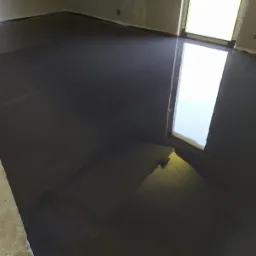 Świeżo wylana, ciemnoszara posadzka przemysłowa w surowym pomieszczeniu, z refleksami światła odbijającymi się od gładkiej powierzchni.