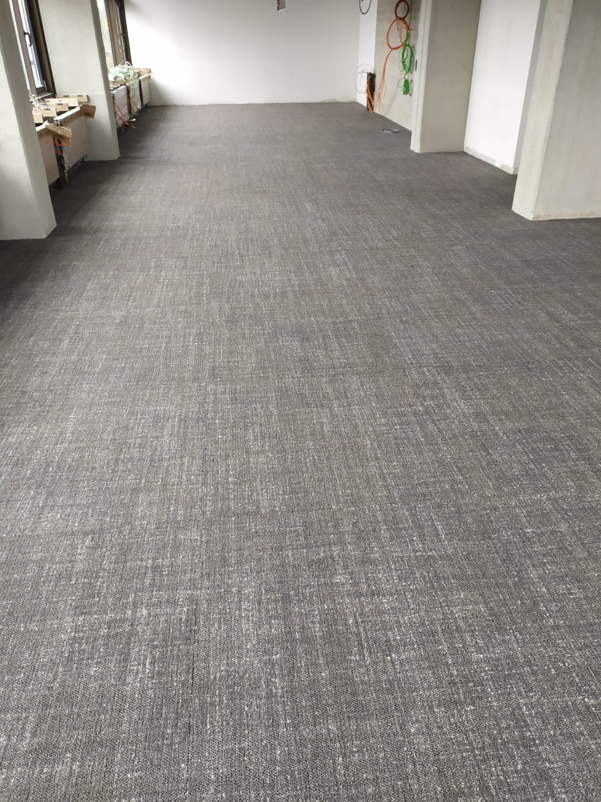 Szara posadzka przemysłowa z delikatnym wzorem w przestronnym, jasnym pomieszczeniu z oknami i widocznymi instalacjami elektrycznymi.