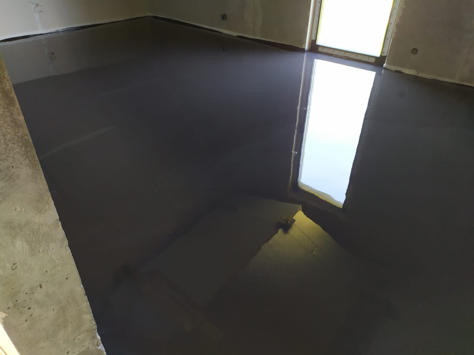 Świeżo wylana, ciemnoszara posadzka przemysłowa w surowym pomieszczeniu, z refleksami światła odbijającymi się od gładkiej powierzchni.