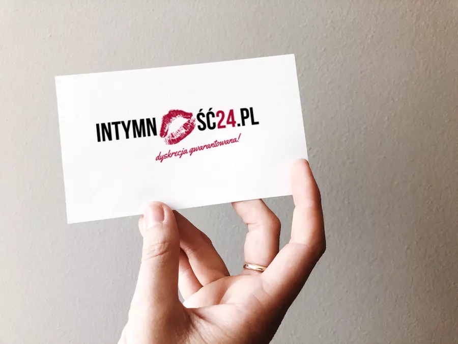 Wizytówka z czarnym napisem INTYMNOSC24.PL i odciskiem ust w kolorze czerwonym, trzymana w dłoni z obrączką na palcu.