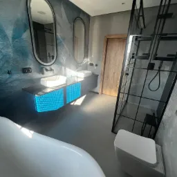 Nowoczesna łazienka z podświetlaną szafką umywalkową, owalnymi lustrami, kabiną prysznicową typu walk-in z czarnymi profilami i wolnostojącą wanną.