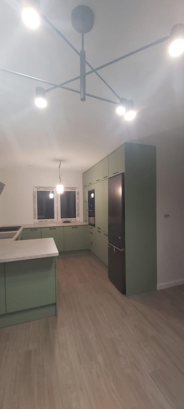 Nowoczesna kuchnia w odcieniach zieleni z drewnianą podłogą, oświetlona designerską lampą sufitową