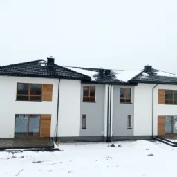 Nowoczesny szeregowiec z czarną dachówką, częściowo pokrytą śniegiem, i drewnianymi okiennicami, widziany w zimowej scenerii.