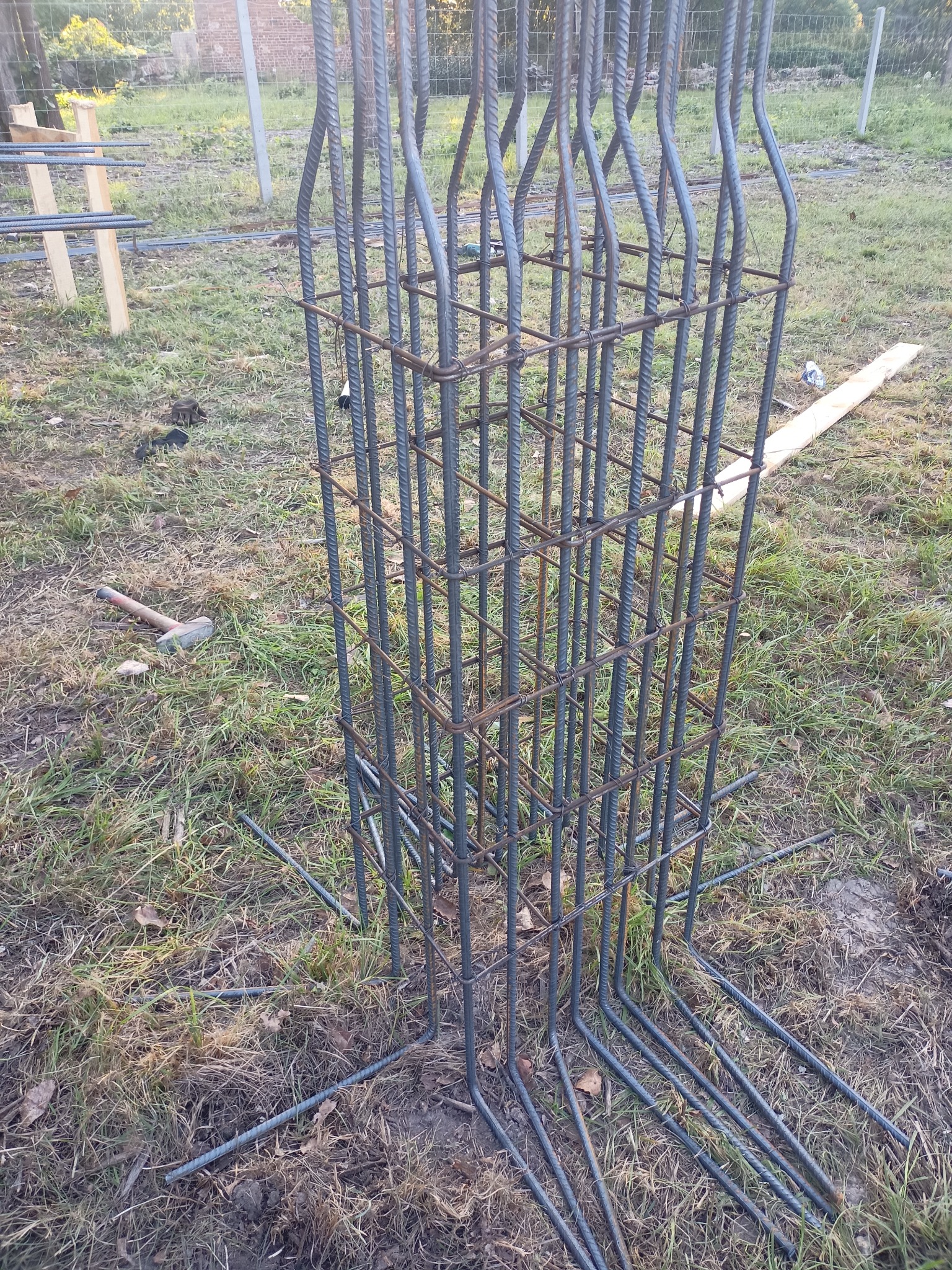 Zbrojenie kolumny fundamentowej z wystającymi prętami, widoczne na trawiastym terenie budowy. Element konstrukcyjny przygotowany do zalania betonem.