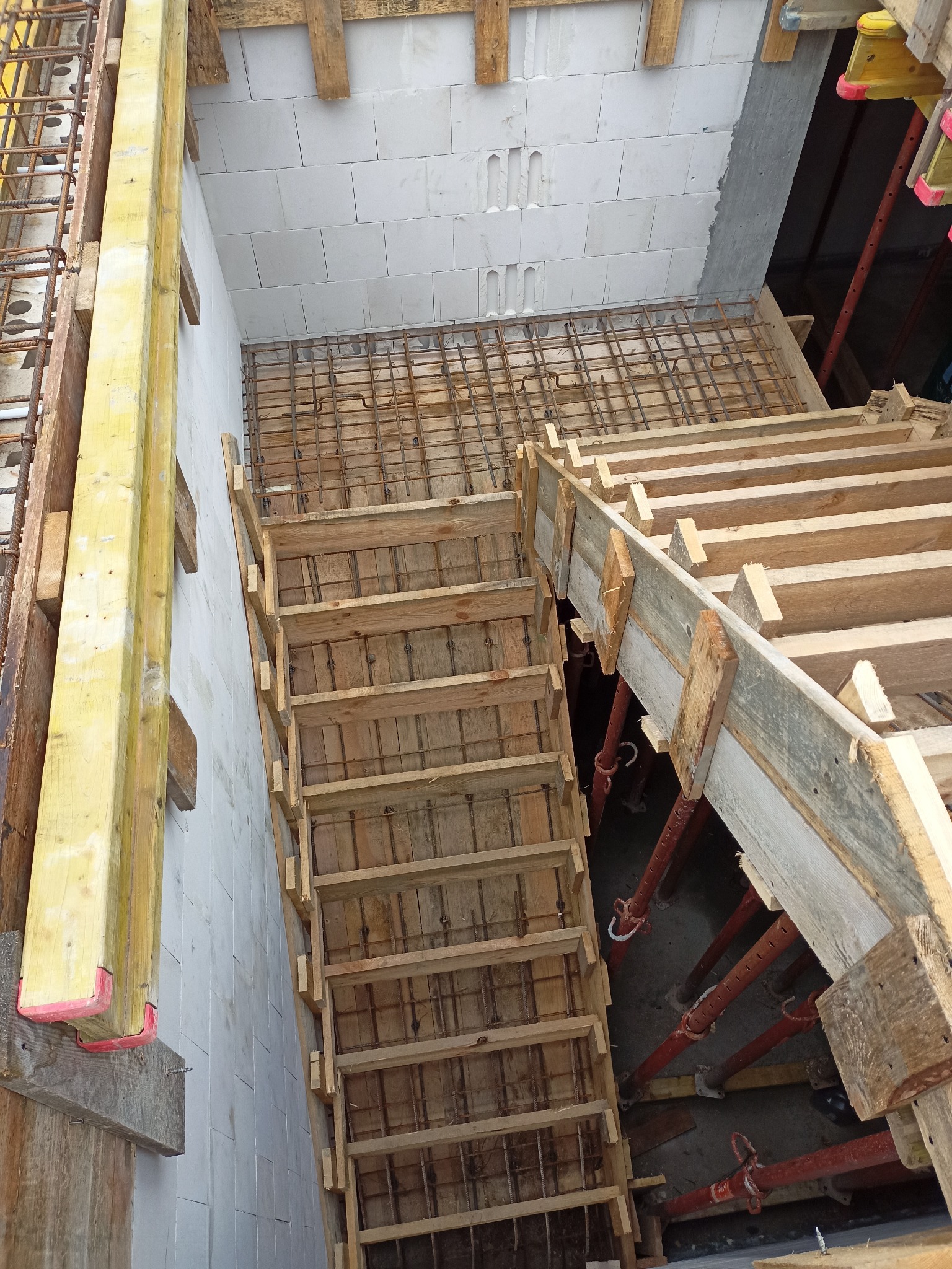 Szczegółowe ujęcie szalunku schodów zbrojonych, widoczne podpory i bloczki betonowe. Etap budowy domu z perspektywy góry.