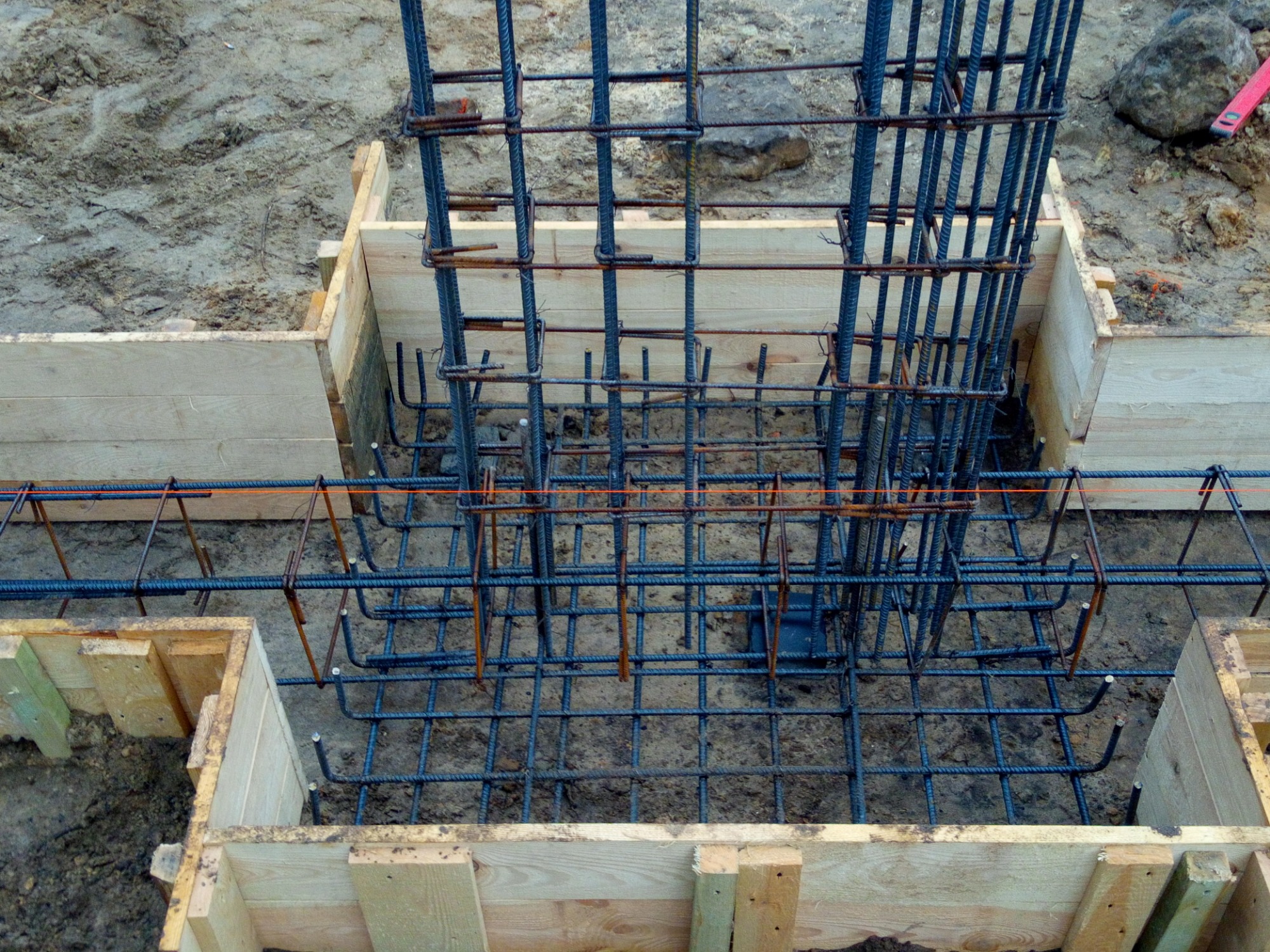 Zbrojenie pionowe i poziome w szalunku drewnianym przygotowane do zalania betonem, widok z góry na wykop.