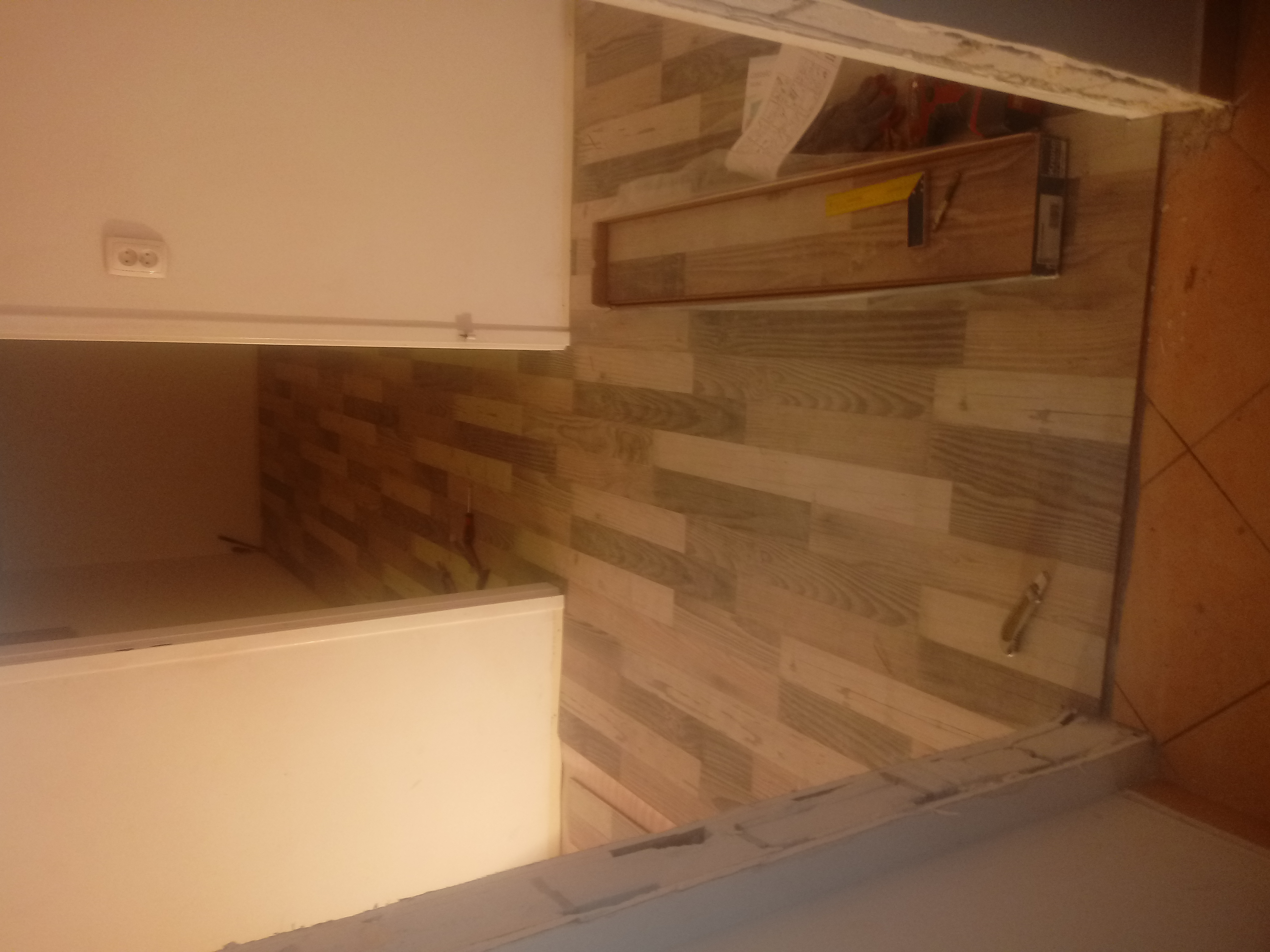 Układanie paneli podłogowych w kuchni, widoczny fragment szafki kuchennej, listwa przypodłogowa w trakcie montażu i paczka paneli.