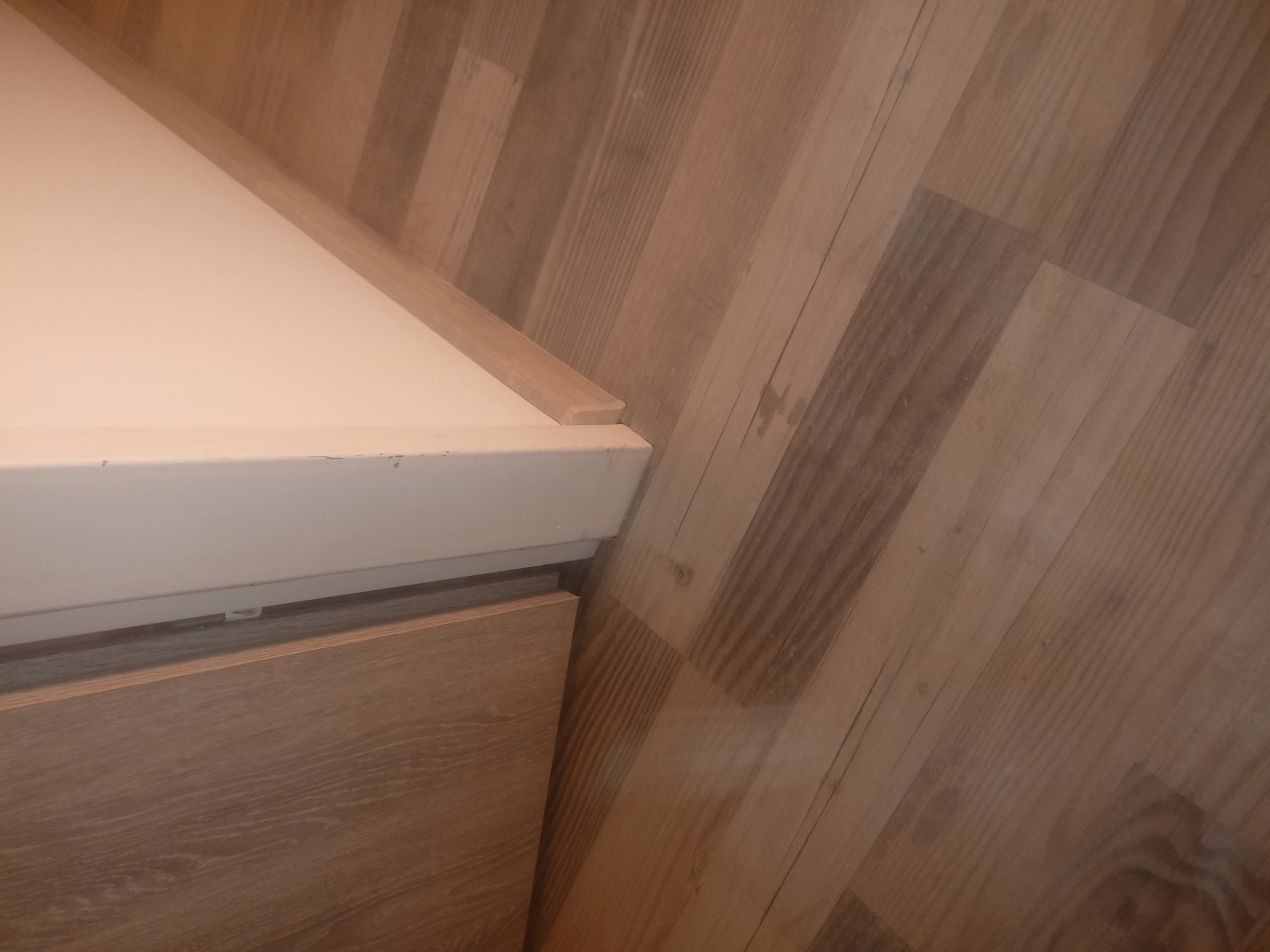 Fragment szafki z drewnianą okleiną i nowo położona podłoga z paneli imitujących drewno, widoczna listwa przypodłogowa.