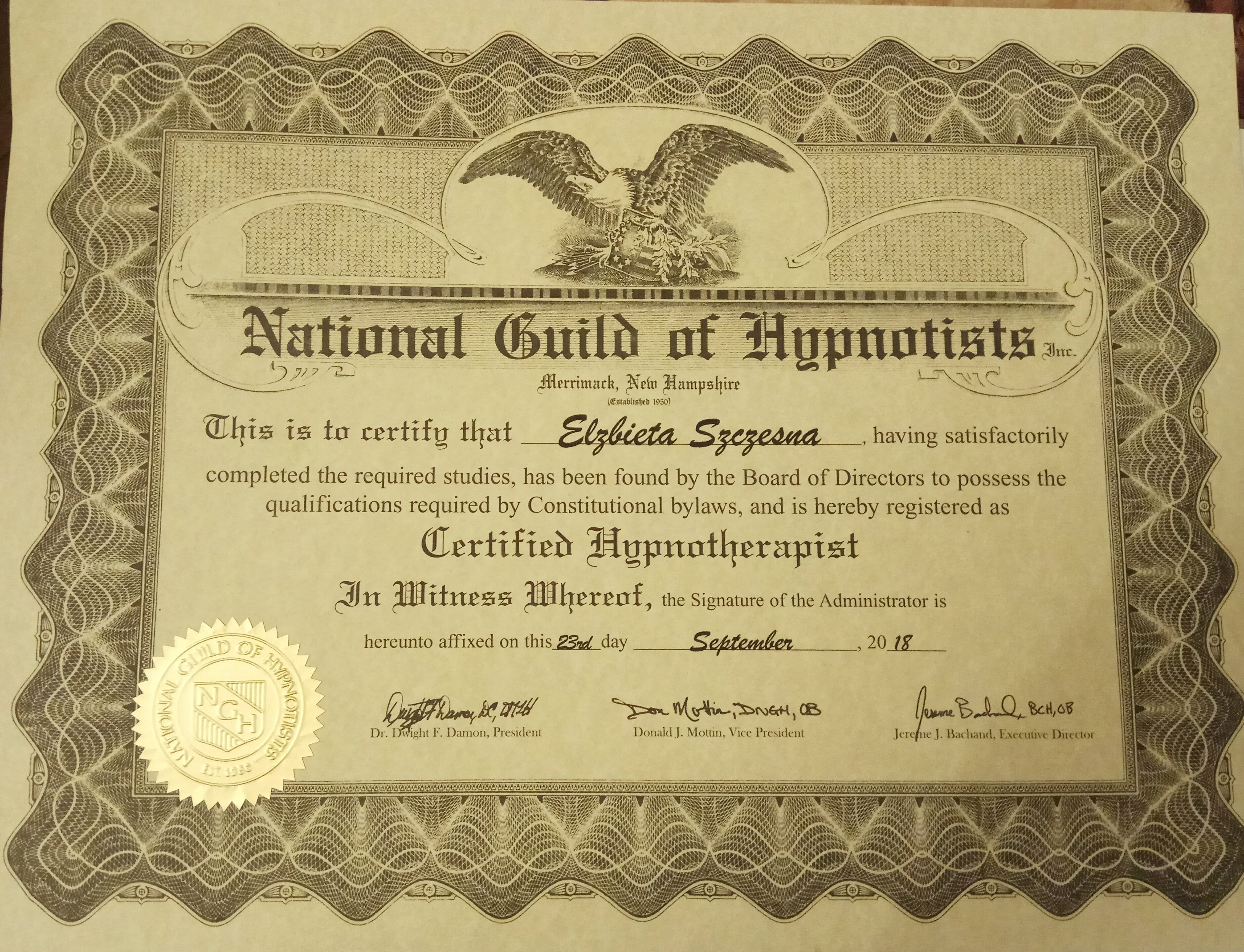 Certyfikat ukończenia kursu hipnoterapii wydany przez National Guild of Hypnotists dla Elżbiety Szczęsnej, z datą 23 września 2018 roku, ozdobiony orłem i złotą pieczęcią.