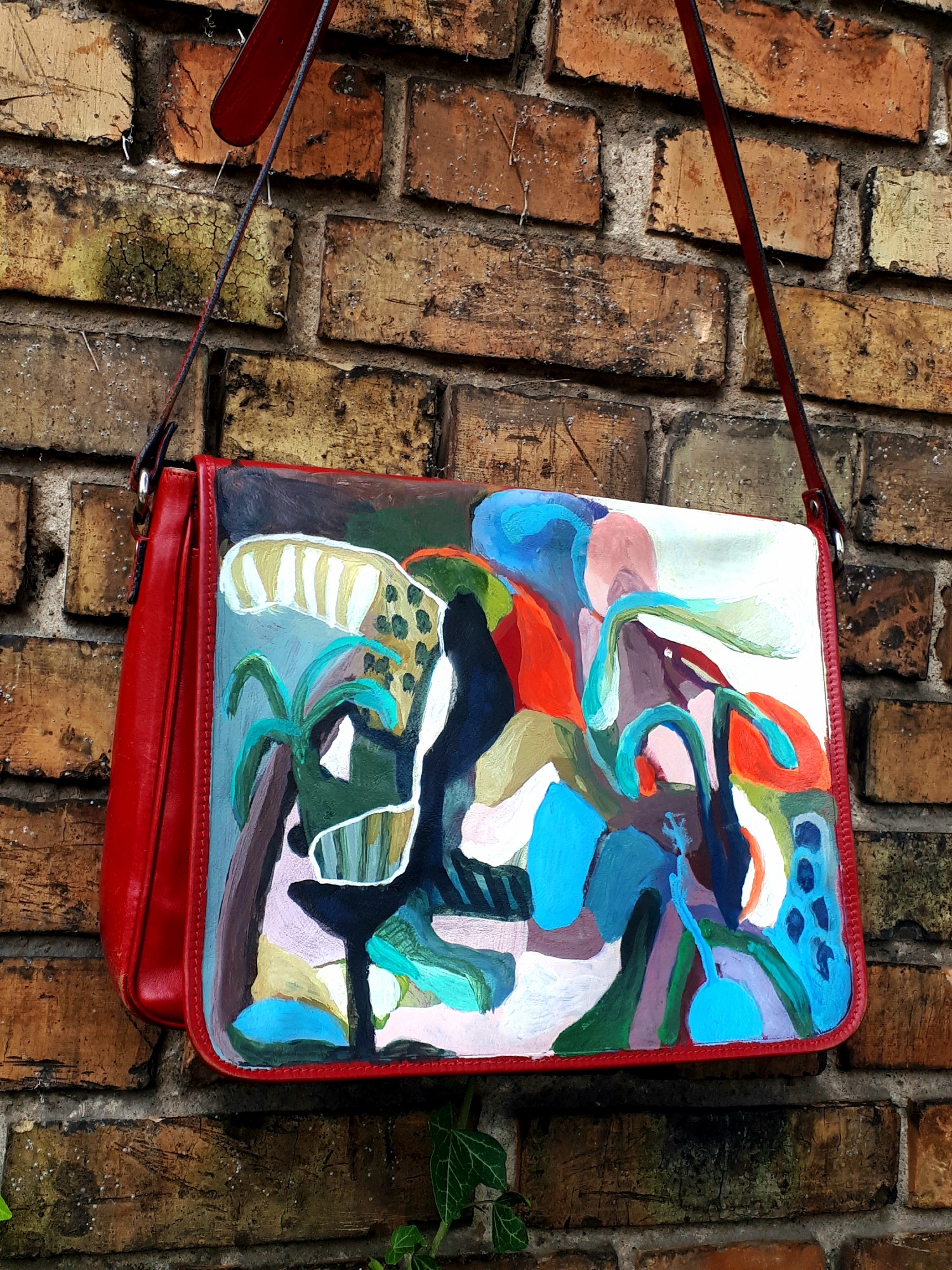Czerwona torba damska z abstrakcyjnym, ręcznie malowanym wzorem, zawieszona na starej, ceglanej ścianie z bliska.