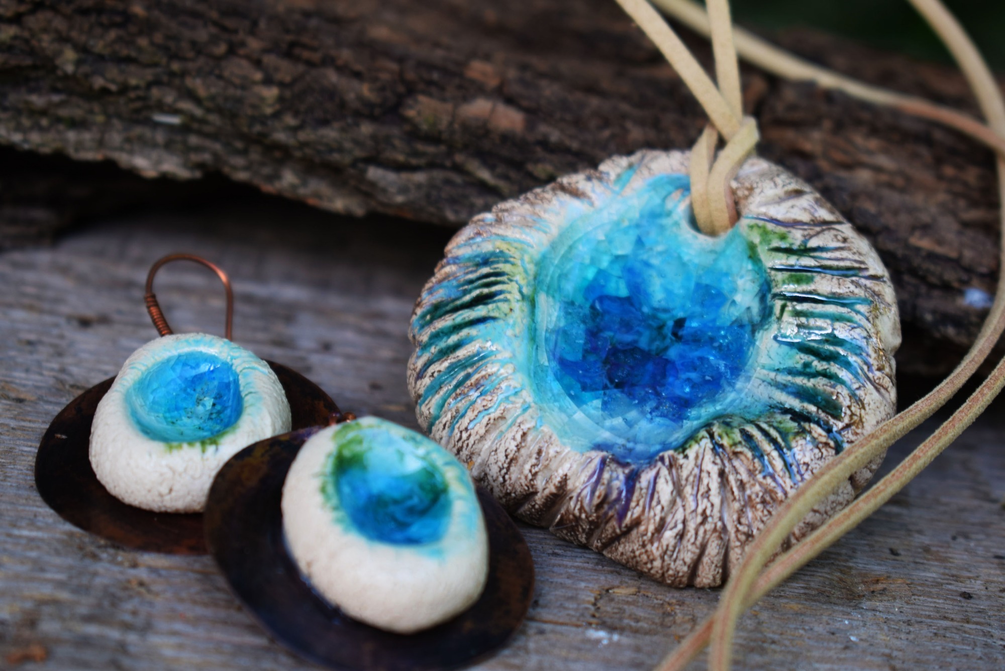 Ręcznie robiona biżuteria ceramiczna: naszyjnik z zawieszką w kształcie nieregularnego kręgu z turkusowym środkiem oraz kolczyki na miedzianych bazach, prezentowane na tle kawałka kory drzewa.