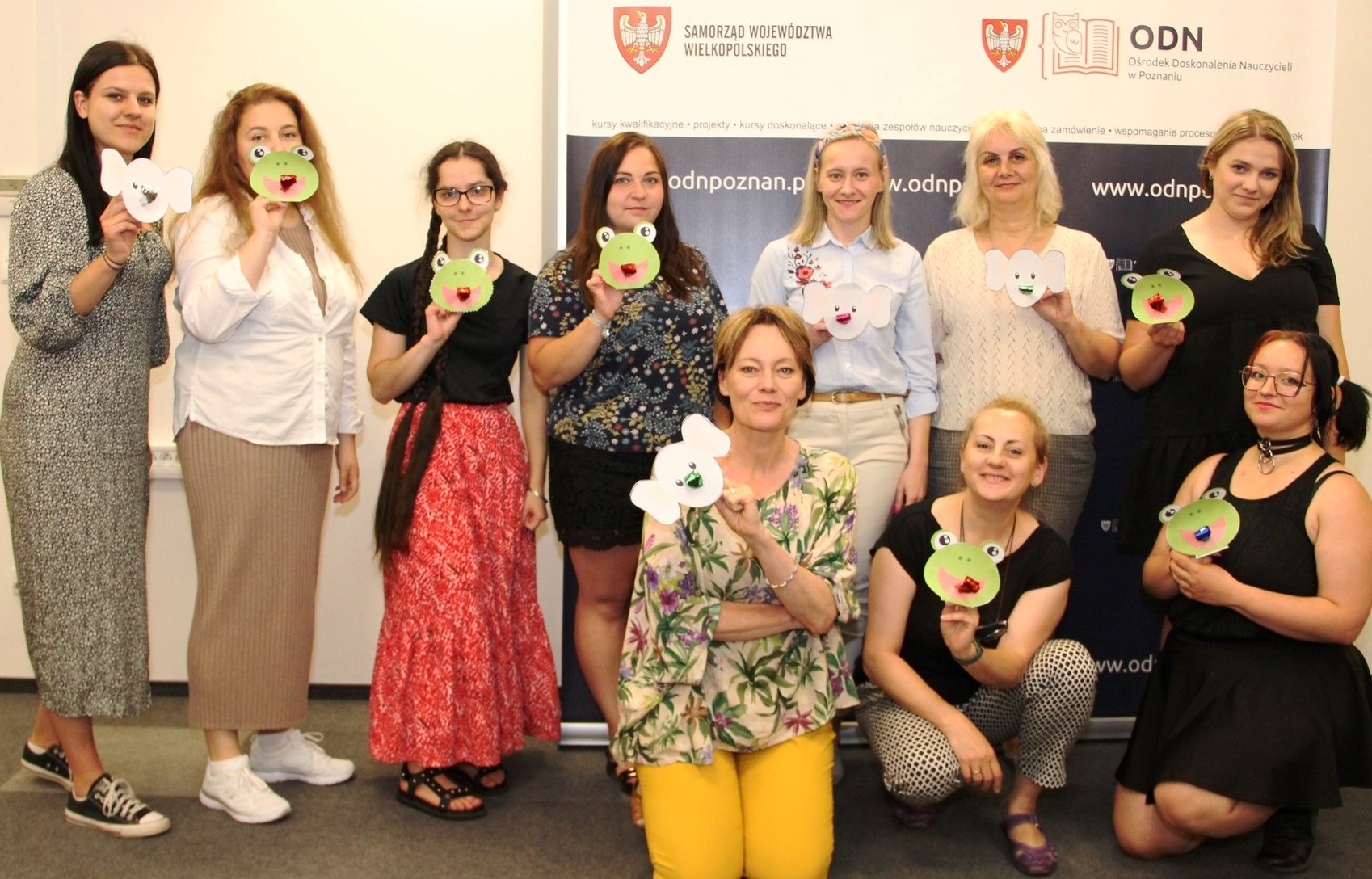 Grupa kobiet prezentuje papierowe maski żab i słoni na tle baneru ODN Poznań podczas profilaktycznych warsztatów.