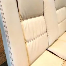 Jasna skórzana kanapa z pikowanymi siedziskami i oparciami, wykończona bordową lamówką i szwami.