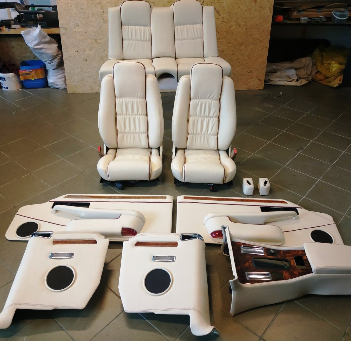 Zestaw odnowionych, kremowych elementów wnętrza samochodowego z brązowymi akcentami: fotele, kanapa tylna, panele drzwiowe z drewnianymi wstawkami i głośnikami.