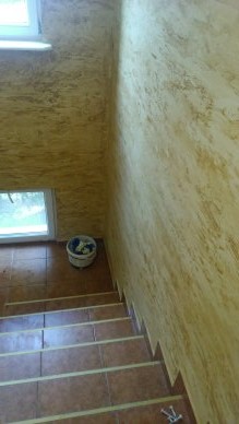 Klatka schodowa po malowaniu ścian z efektem dekoracyjnym, widoczne brązowe płytki na schodach i wiadro z farbą w rogu.