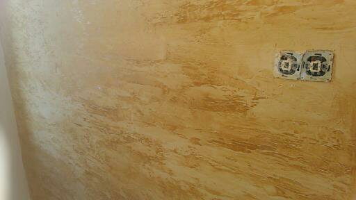 Ściana z dekoracyjną, beżowo-złotą fakturą, z widocznymi gniazdkami elektrycznymi bez osprzętu.