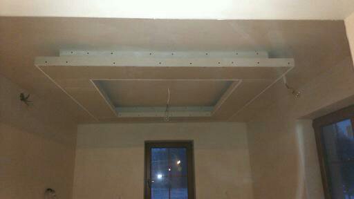Sufit podwieszany z płyt kartonowo-gipsowych w trakcie montażu, widoczne przewody elektryczne i niedoskonałości wykończenia ścian.