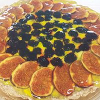 Tarta z figami i jeżynami na żółtym kremie, ułożona na ozdobnej podkładce.