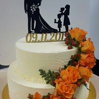 Dwupiętrowy tort weselny z białym kremem, ozdobiony pomarańczowymi różami i czerwonymi owocami, z topperami przedstawiającymi sylwetki pary młodej i rodziny z dzieckiem, data 09.11.2019.