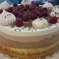 Tort trójwarstwowy z kremem czekoladowym, białym i beżowym, udekorowany malinami, bezami i startą czekoladą.