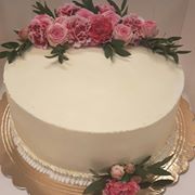 Tort śmietankowy z dekoracją z różowych róż i zielonych gałązek, umieszczony na złotej podkładce.