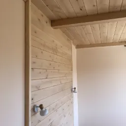 Wykończone wnętrze z drewnianą boazerią ścienną i sufitową, uzupełnione kinkietami w stylu retro, kontrastujące z gładką, pomalowaną ścianą w odcieniu kremowym.