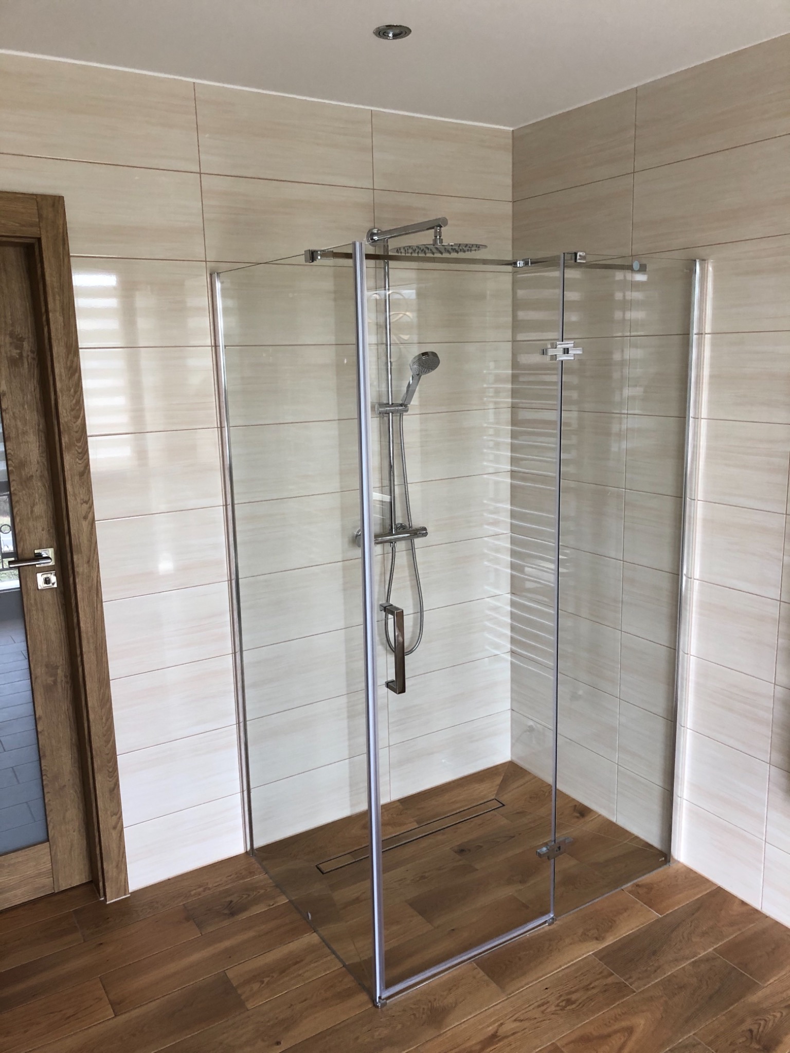 Kabina prysznicowa ze szklanymi ściankami, chromowaną armaturą i odpływem liniowym w podłodze wyłożonej panelami w Raba Wyżna.