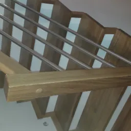 Drewniane schody ze stalowymi relingami, widok z dołu, ukazujący strukturę drewna i minimalistyczny design.