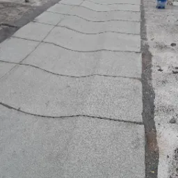 Fragment płaskiego dachu po naprawie, z widocznymi łatami papy bitumicznej i butlą gazową w tle.